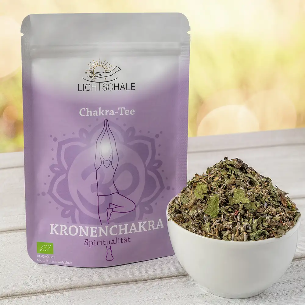 Vorderseite der Verpackung des Kronenchakra-Tees von Lich Schale. Lila Tüte mit der Aufschrift ‚Chakra-Tee – Kronenchakra – Spiritualität‘. Im Zentrum ist eine stilisierte Person in der Yoga-Pose Vrksasana (Baumhaltung) mit erhobenen Armen abgebildet. Im Hintergrund ein Mandala mit dem Om-Symbol. Daneben eine weiße Schale mit einer Mischung aus getrockneten Kräutern. Unten links das EU-Bio-Logo.