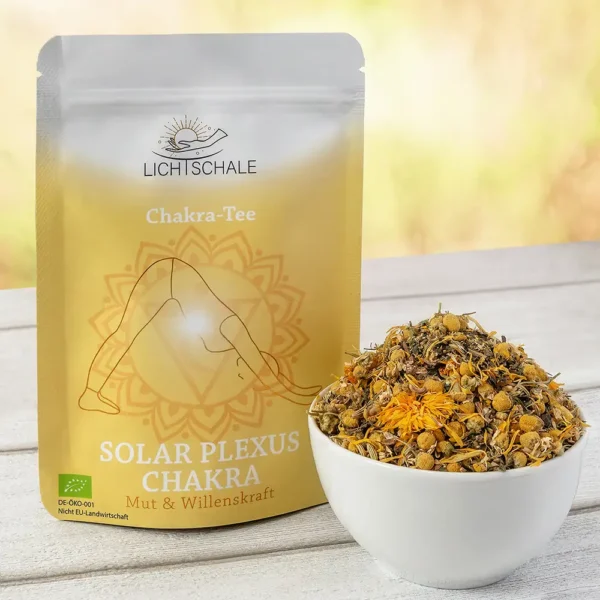 Vorderseite der Verpackung des Solar Plexus Chakra-Tees von Lich Schale. Gelb-goldenes Design mit einer Figur in Yoga-Pose (Herabschauender Hund), im Hintergrund das Solarplexus-Chakra-Symbol. Darunter die Aufschrift: ‚Solar Plexus Chakra – Mut & Willenskraft‘. Daneben eine weiße Schale mit einer Kräutermischung, sichtbar sind Kamillenblüten und andere getrocknete Pflanzenbestandteile. Bio-Siegel links unten.