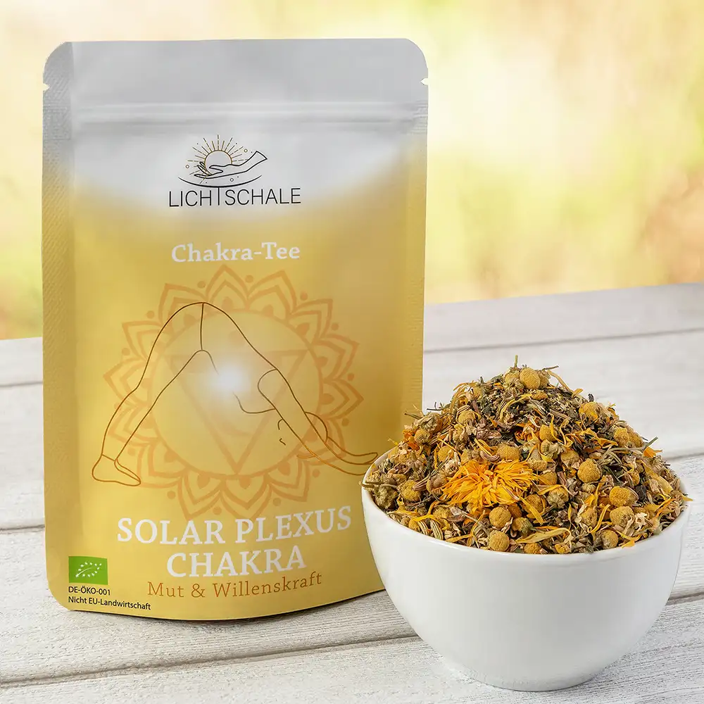 Vorderseite der Verpackung des Solar Plexus Chakra-Tees von Lich Schale. Gelb-goldenes Design mit einer Figur in Yoga-Pose (Herabschauender Hund), im Hintergrund das Solarplexus-Chakra-Symbol. Darunter die Aufschrift: ‚Solar Plexus Chakra – Mut & Willenskraft‘. Daneben eine weiße Schale mit einer Kräutermischung, sichtbar sind Kamillenblüten und andere getrocknete Pflanzenbestandteile. Bio-Siegel links unten.