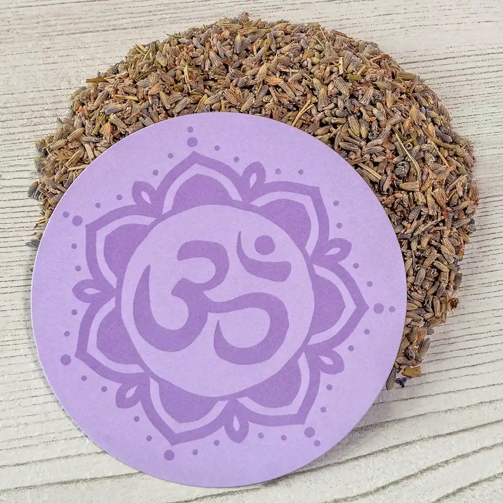 Runder, violetter Untersetzer mit dem Symbol des Kronenchakras (Sahasrara), liegend auf hellem Holz, umgeben von getrockneten Lavendelblüten
