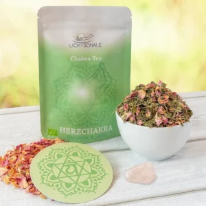 Chakra-Tee-Set für das Herzchakra mit grüner Verpackung, weißer Schale mit Kräutern und Rosenblüten, passender runder Unterlage mit Anahata-Symbol und einem rosa Heilstein (Rosenquarz) auf hellem Holzuntergrund