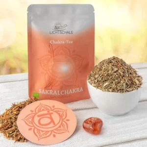 Orangenes Chakra-Tee-Set für das Sakralchakra mit Teepackung, weißer Schale voller Kräutermischung, runder Unterlage mit Svadhisthana-Symbol und orangefarbenem Heilstein (Karneol) auf hellem Holztisch