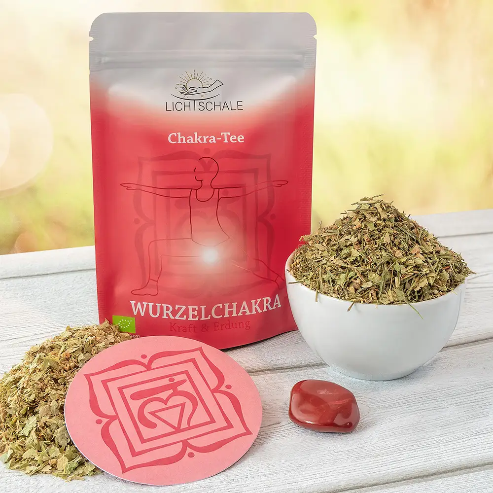 Rotes Chakra-Tee-Set für das Wurzelchakra mit Teepackung, weißer Schale voller Kräutermischung, runder Unterlage mit Muladhara-Symbol und rotem Heilstein (Jaspis) auf hellem Holztisch